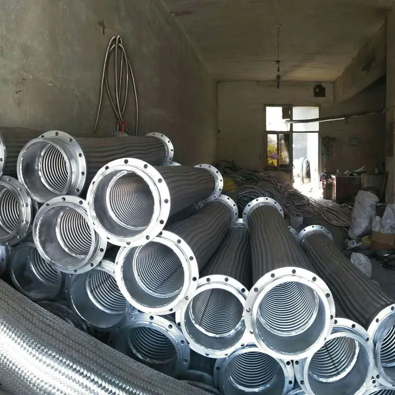 Large-diameter corrugated metal hoses with flanged ends stacked in a workshop